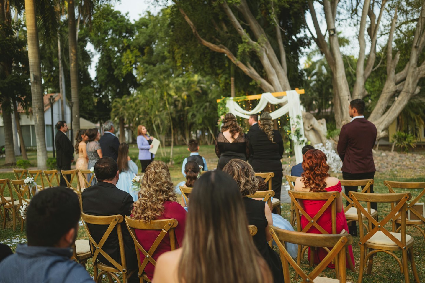 Outdoor wedding ceremony with guests seated facing a decorated arch.