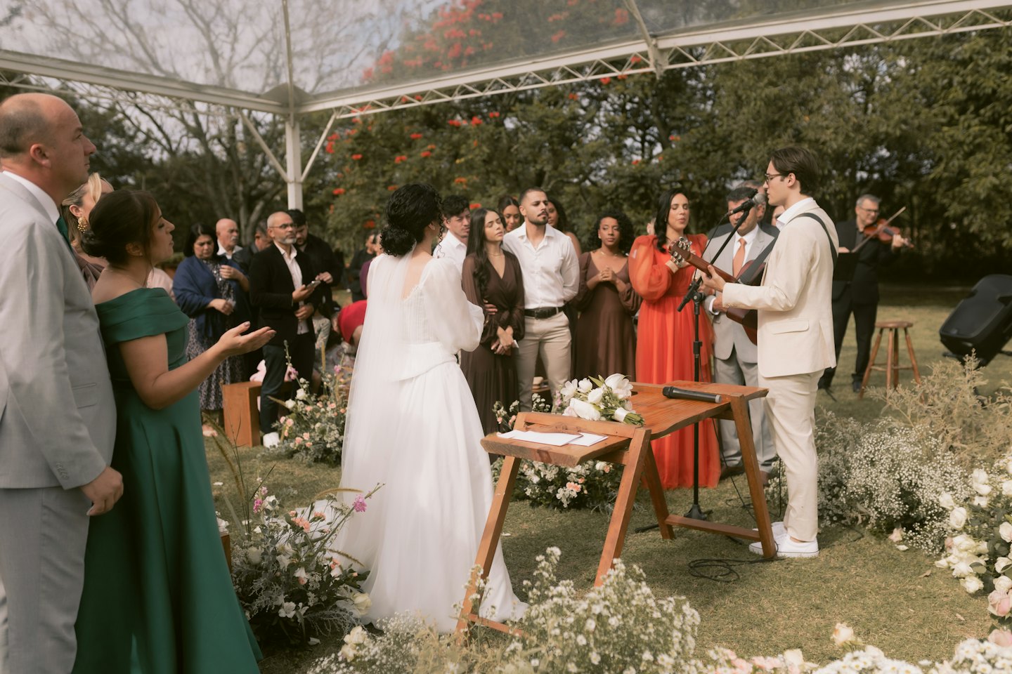 A man plays guitar and sings at an outdoor wedding.