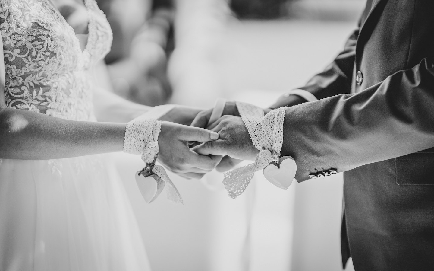 A couple holds hands with lace ribbons tied around their wrists.