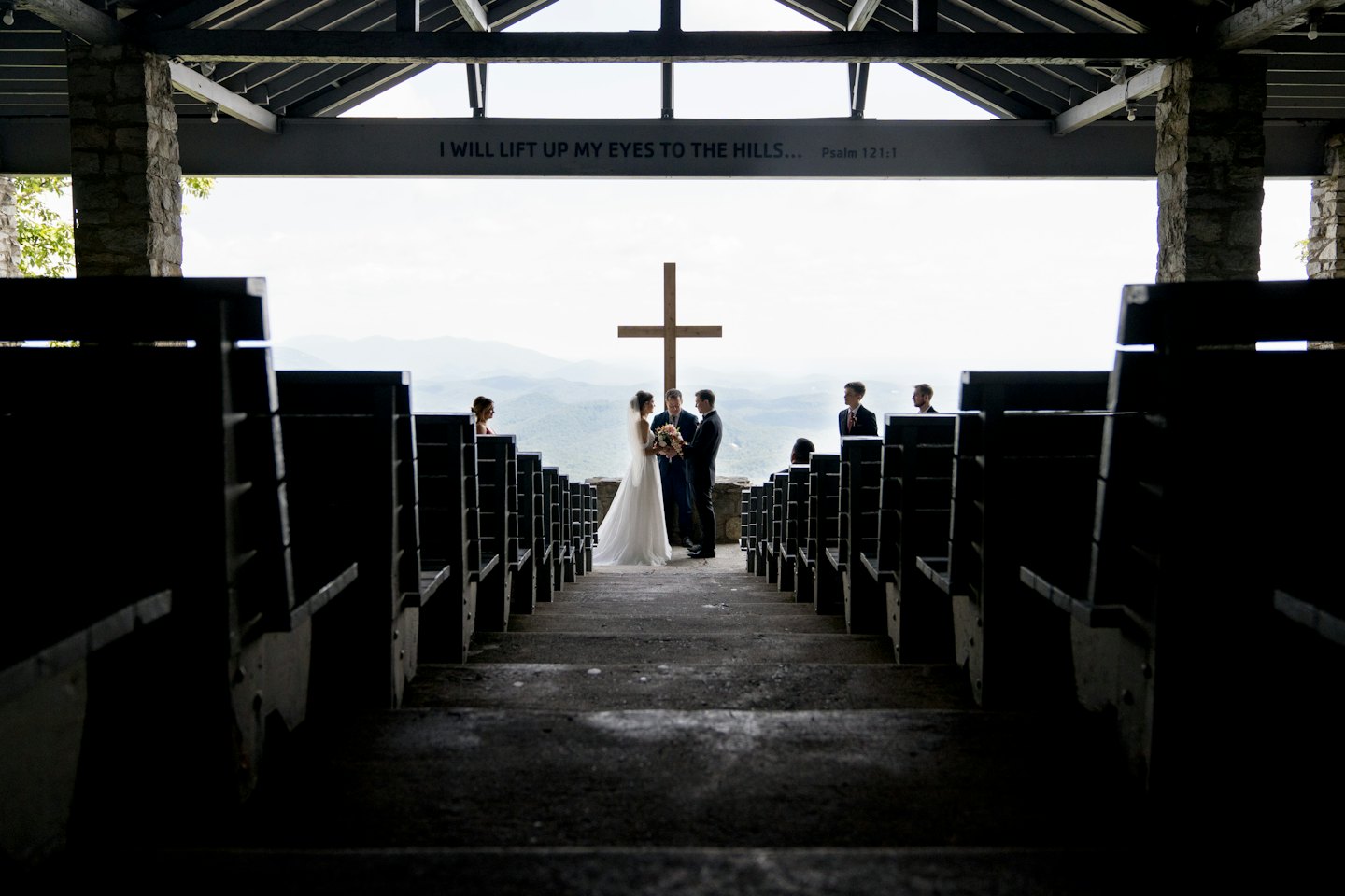 Bride and groom standing before a wooden cross at a mountain wedding.